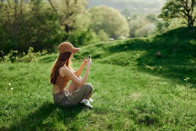 Una mujer sentada en la hierba verde en un parque en verano contra un paisaje de árboles, el trabajo de un freelancer y blogger