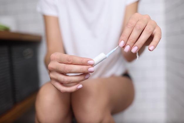 Mujer sentada en el inodoro y sosteniendo un tampón higiénico en sus manos Concepto de menstruación en mujeres