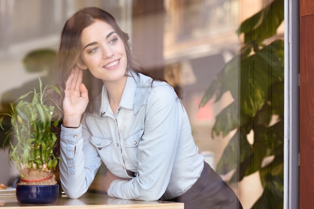 Mujer sentada en el interior de café urbano mirando por la ventana