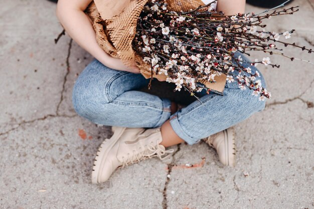 mujer sentada en jeans azules sosteniendo un gran ramo de ramas con flores de cerezo rosadas en flor