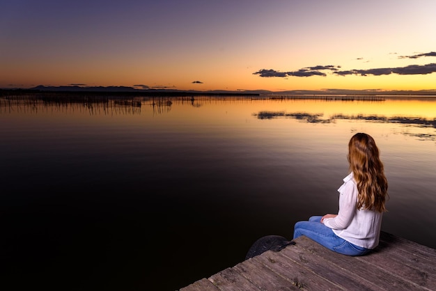 Foto mujer sentada junto al lago contra el cielo durante la puesta de sol