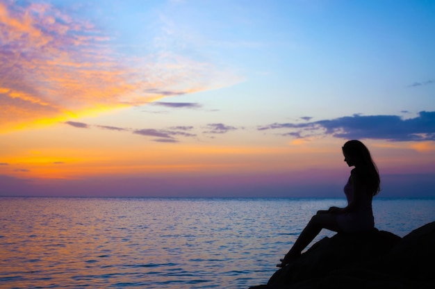 Foto mujer sentada junto al mar contra el cielo durante la puesta de sol