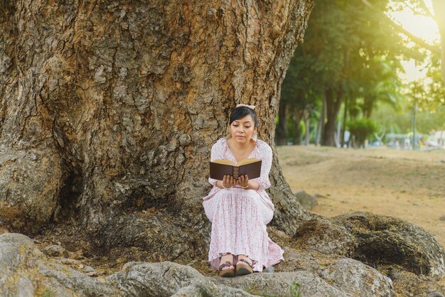 Mujer sentada junto a un tronco de árbol en un parque leyendo un libro Día Mundial del Libro Concepto de la lectura