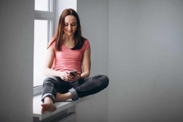 Mujer sentada junto a la ventana con el teléfono