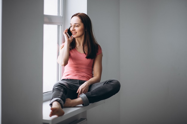 Mujer sentada junto a la ventana con el teléfono