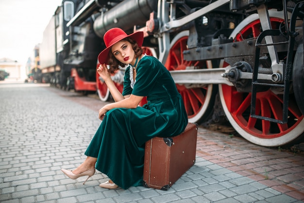 Mujer sentada en la maleta contra el tren de vapor