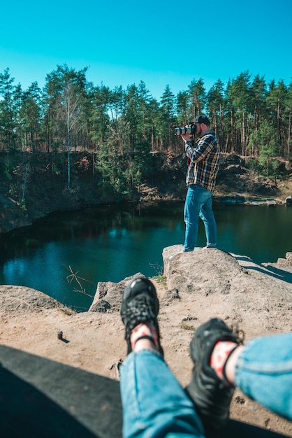 Mujer sentada en el maletero del coche hombre tomando fotos en el lago de la cámara profesional en el concepto de viaje de fondo