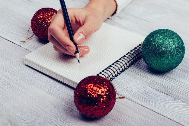 Mujer sentada en una mesa con bolas navideñas y escribiendo en un cuaderno con un lápiz