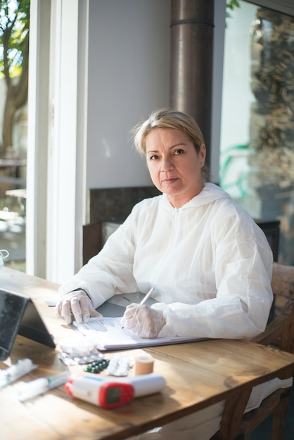 Una mujer sentada en una mesa en un café, vestida con una camisa blanca y guantes, escribe en un papel.