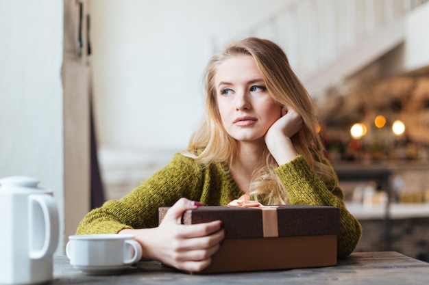 Mujer sentada en la mesa con caja de regalo y esperando a alguien