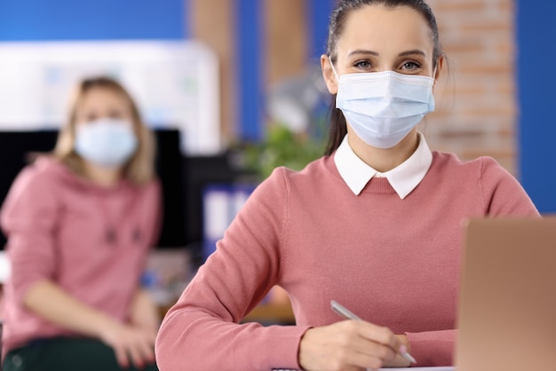 Mujer sentada a la mesa con máscara médica protectora. Trabajo en equipo durante el concepto de pandemia de covid-19