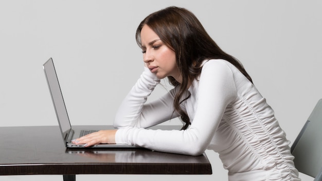 Mujer sentada a la mesa, mirando y trabajando en la computadora portátil, aislado. Postura incorrecta, alterada, defecto de la escoliosis.