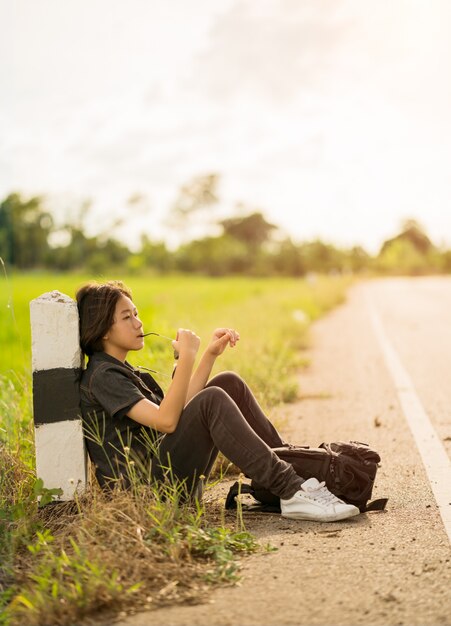Foto mujer sentada con mochila haciendo autostop a lo largo de una carretera en el campo