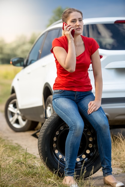 Mujer sentada en el neumático de repuesto al borde de la carretera y pidiendo ayuda