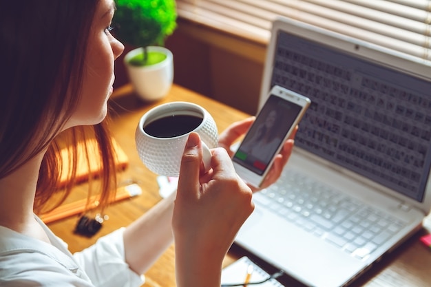 Mujer sentada en la oficina en casa con una taza de café y teléfono