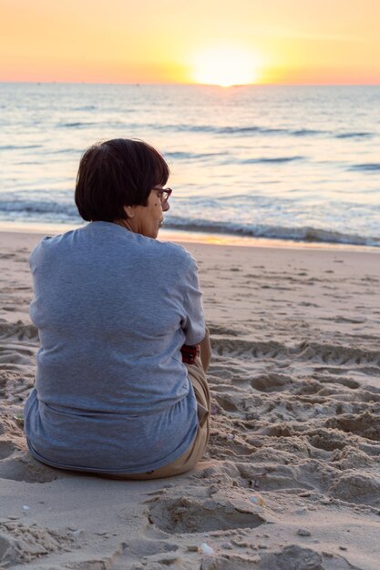 Foto mujer sentada en la orilla de la playa contra el cielo durante la puesta de sol