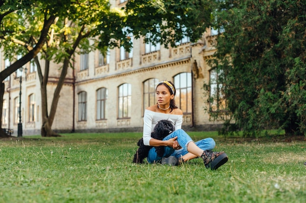 mujer sentada en el parque en el césped con un lindo perro negro y mira hacia otro lado con una cara seria
