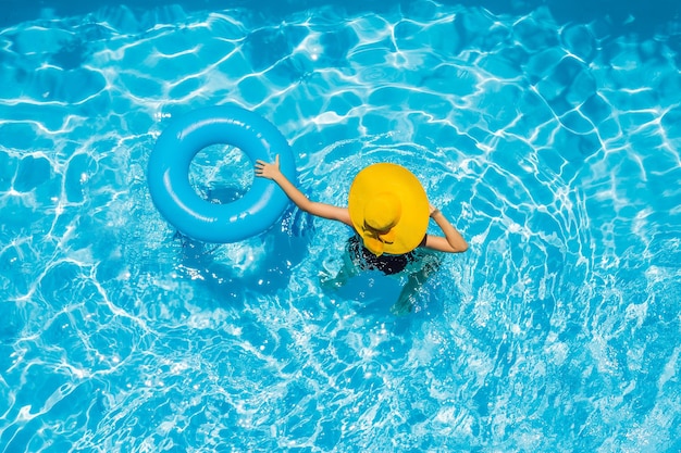 Mujer sentada en una piscina en un flotador de piscina de anillo en un gran sombrero amarillo