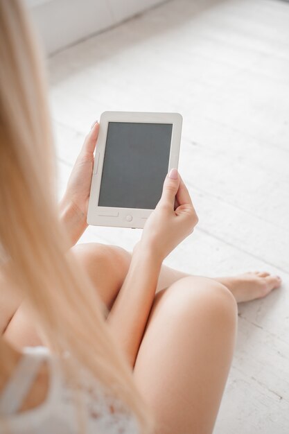 Mujer sentada en el piso blanco y sosteniendo un libro electrónico en sus manos