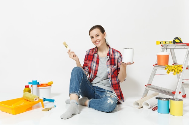 Mujer sentada en el piso con pincel, lata de pintura, instrumentos para la habitación del apartamento de renovación aislado sobre fondo blanco. Papel pintado, accesorios para pegar, herramientas de pintura. Reparar el concepto de hogar. Copia espacio