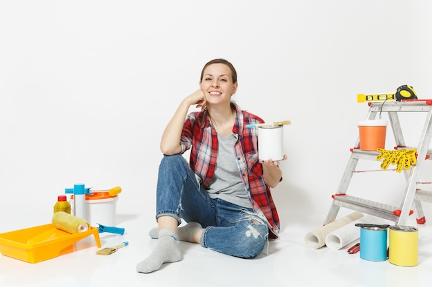 Mujer sentada en el piso con pincel, lata de pintura, instrumentos para la habitación del apartamento de renovación aislado sobre fondo blanco. Papel pintado, accesorios para pegar, herramientas de pintura. Reparar el concepto de hogar. Copia espacio