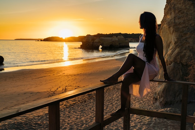 Foto mujer sentada en una pista de aterrizaje mirando el atardecer en la playa en algarve, portugal