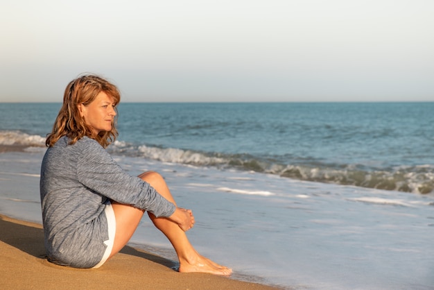 Mujer sentada en la playa, admirando el paisaje del océano