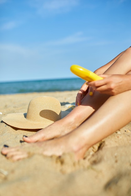 Mujer sentada en la playa de arena poniéndose crema solar en la piel