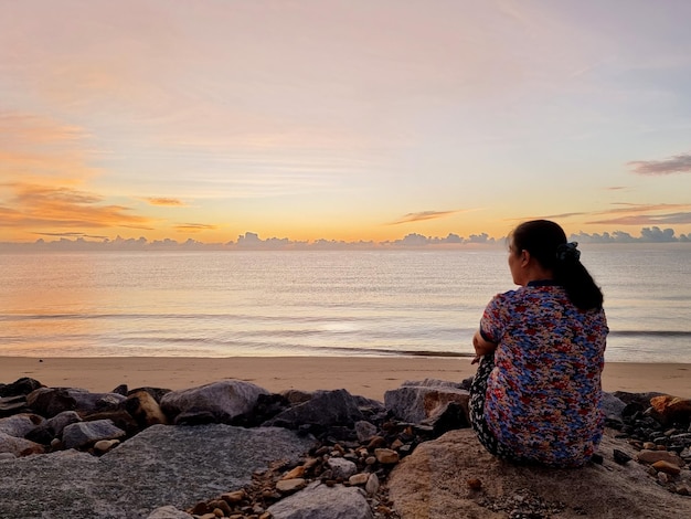 La mujer sentada en la playa esperando ver el amanecer en el hermoso mar con cielo