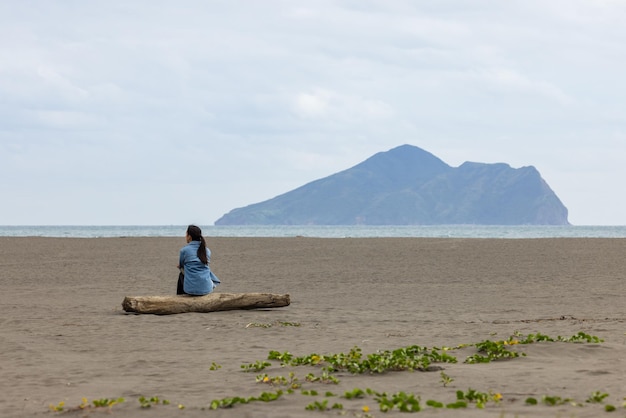 Mujer sentada en la playa y mirando el Guishan en Yilan