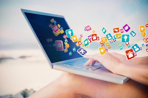 Mujer sentada en la playa usando su computadora portátil con aplicaciones informáticas coloridas