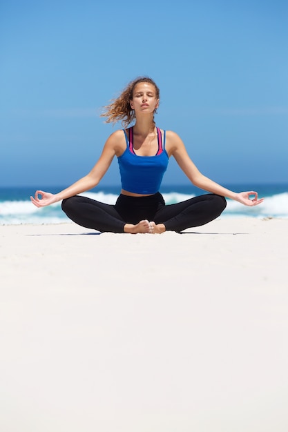 Mujer sentada en posición de yoga en la playa