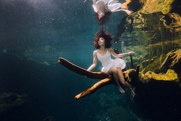 Foto mujer sentada en una rama bajo el agua