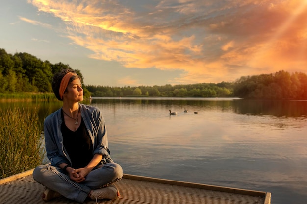 Mujer sentada y relajada al borde de un lago al atardecer