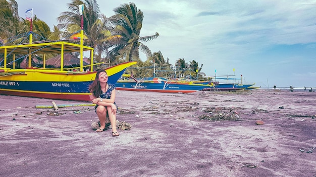 Mujer sentada en una roca contra los barcos en la playa