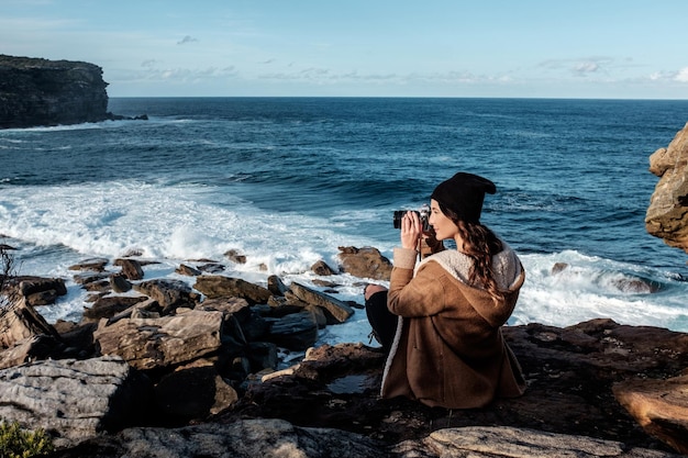 Mujer sentada en una roca junto al mar contra el cielo en un día soleado