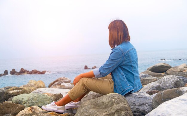 Foto mujer sentada en una roca junto al mar contra el cielo