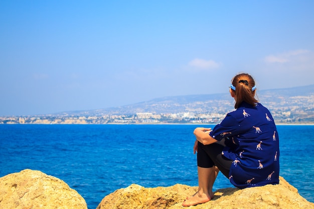 Mujer sentada en la roca y mirando el fondo del mar.