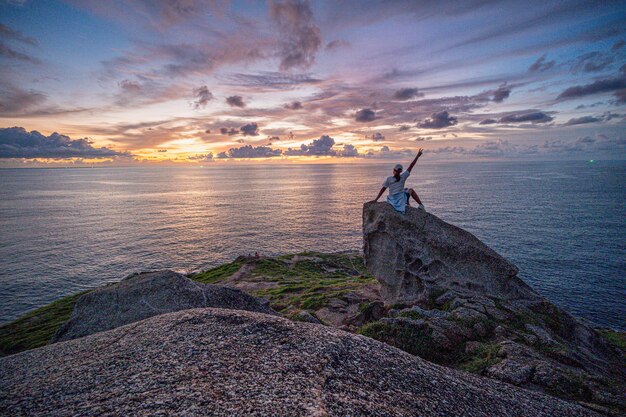 Mujer sentada en una roca y viendo la puesta de sol sobre el océano en la isla de Phuket en el verano de Tailandia