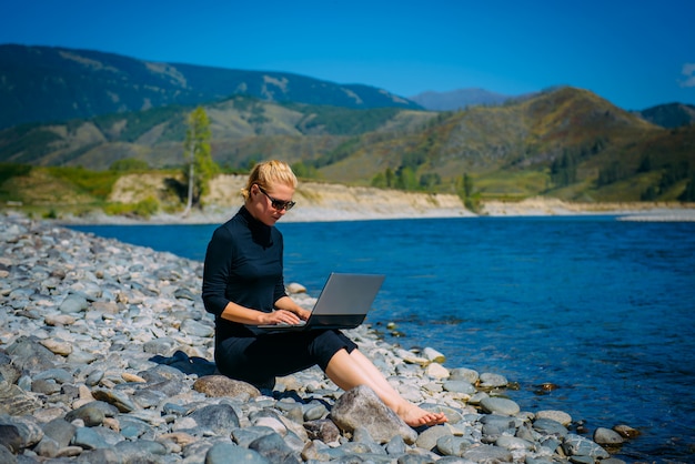 Mujer sentada en las rocas usando una computadora portátil