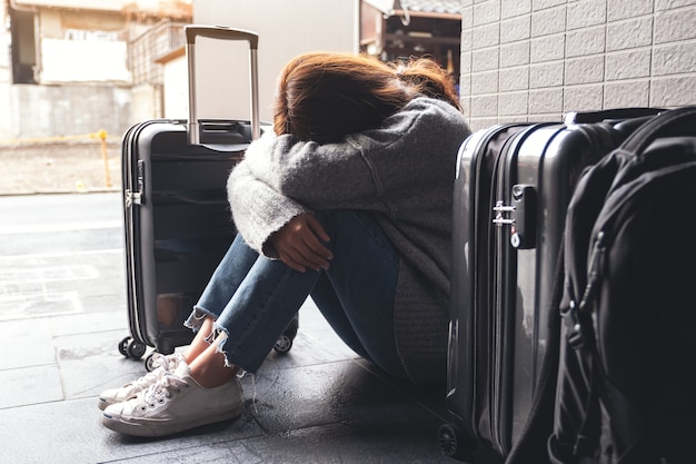 Una mujer sentada con sentimiento de tristeza mientras viaja con una gran cantidad de equipaje en el suelo