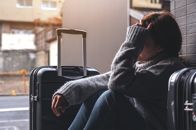 Una mujer sentada con sentimiento de tristeza mientras viaja con una gran cantidad de equipaje en el suelo