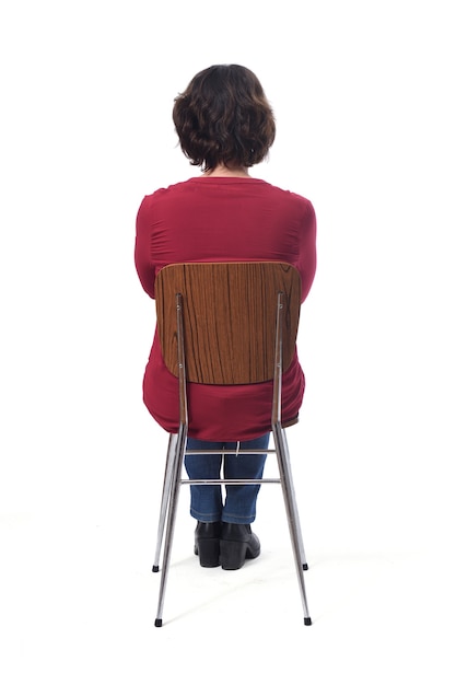 Mujer sentada en una silla con la espalda sobre fondo blanco, con los brazos cruzados.