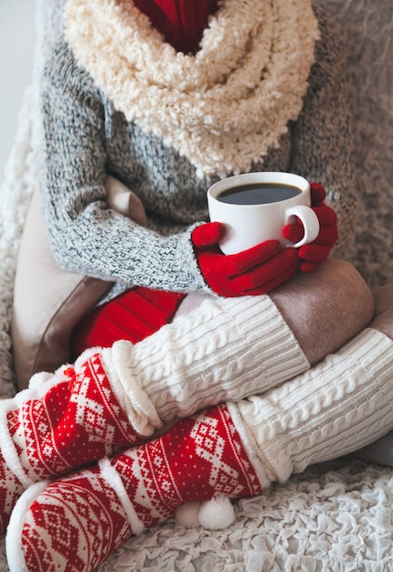 Mujer sentada en la silla en la habitación luminosa con una taza de café en las manos en Navidad,