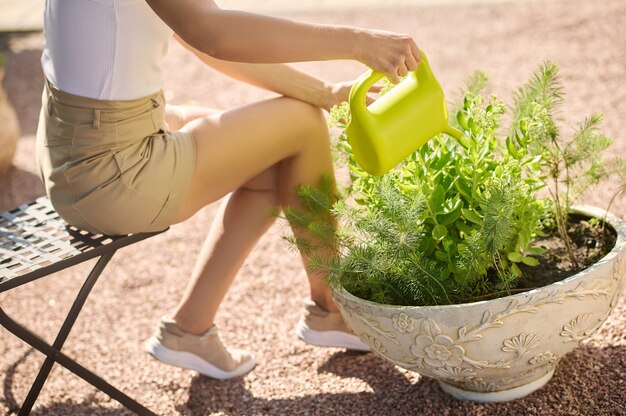 Mujer sentada en una silla de jardín regando las flores