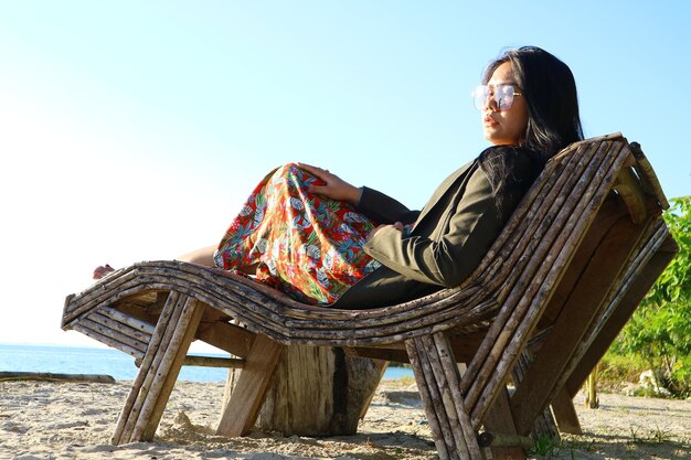 Foto mujer sentada en una silla en la playa contra un cielo despejado