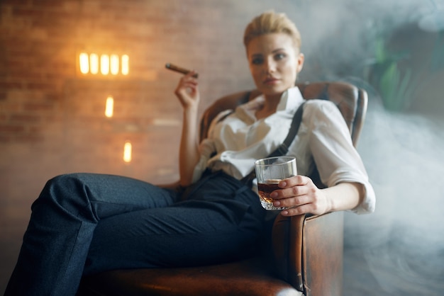 Mujer sentada en una silla con whisky y cigarro