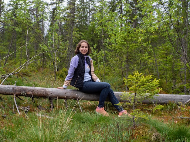 Mujer sentada sobre un árbol caído en un bosque verde