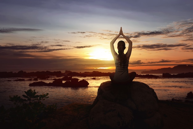 Mujer sentada sobre la roca haciendo yoga