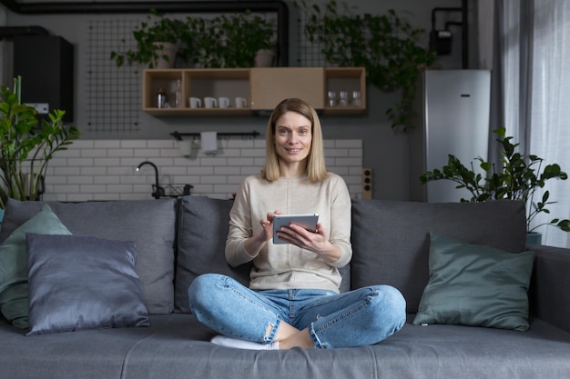 Mujer sentada en un sofá en casa usando una tableta leyendo libros electrónicos y aprendiendo en línea